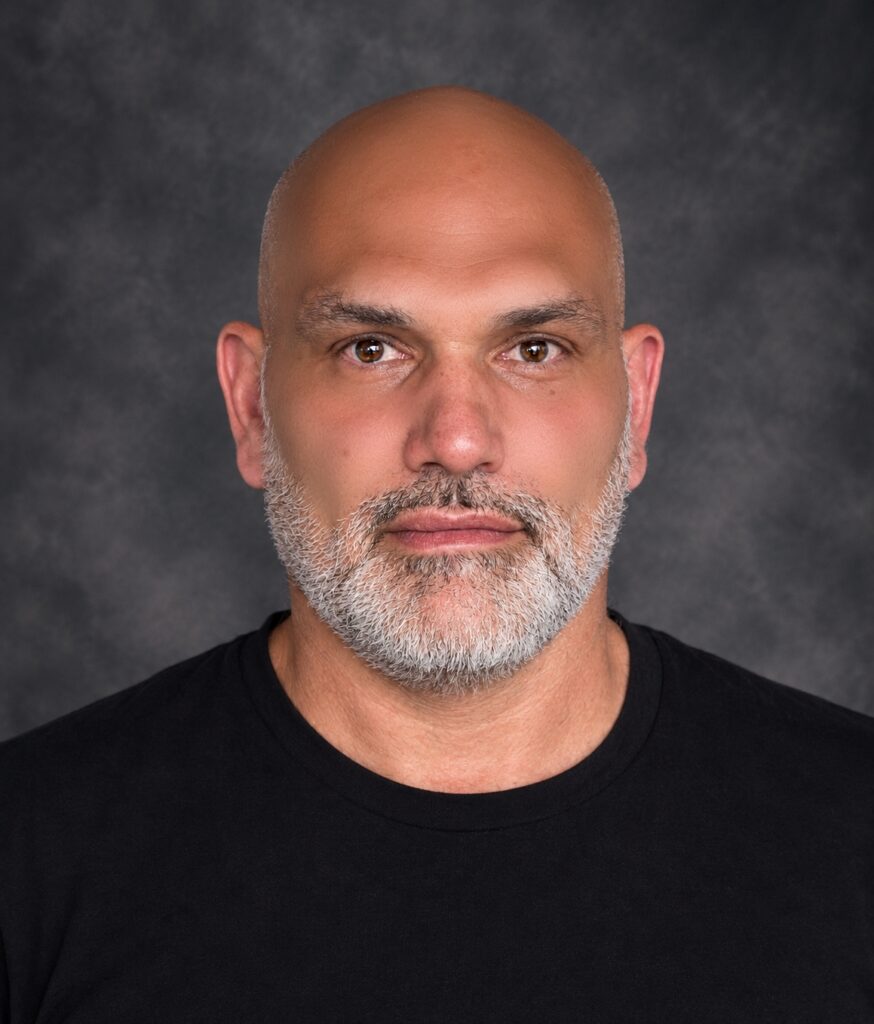 Official biography portrait of electronic music producer and composer Philippe JOUMARD, featuring a close-up profile view with a grey beard against a dark textured background.